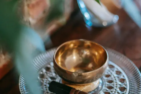 A golden singing bowl and mallet on a wooden table with a plant nearby